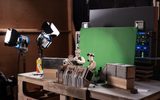 Claymation figures and sets are placed in front of a green screen on a studio table, with professional lights and equipment in the background, ready for filming.