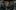 A large group of people sit on benches and the floor in a dark room, watching a wall and floor projection of numerous black-and-white and colour portraits and images, creating an immersive visual experience.