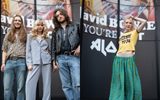 Three people in retro outfits stand in front of a mural of David Bowie on the left; on the right, a person in a yellow Bowie 1974 crop top and green skirt poses in front of the same mural.
