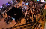 A large group of people gather at an indoor tech event with stands and exhibits. A colourful sign on the wall reads “SETS 2024 - New Entertainment Technology Summit - London.”.